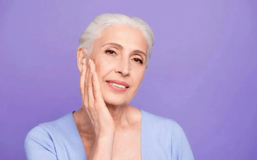 A woman with white hair is holding her face.