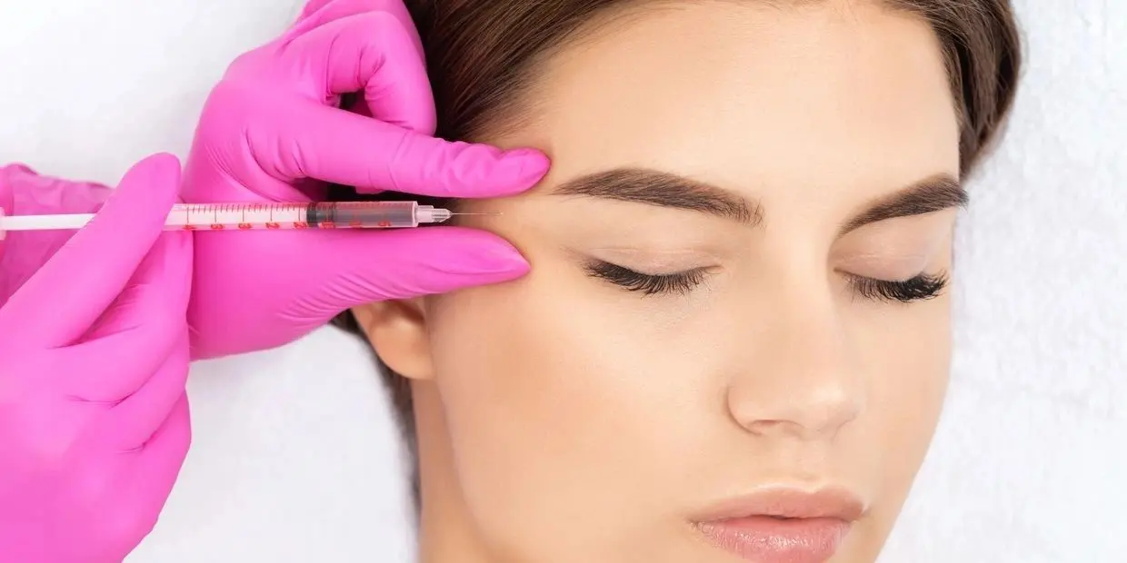 A woman getting her eyebrows threaded by an esthetician.